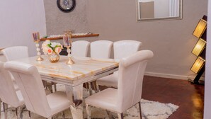 A dining area with a marble table, white upholstered chairs, a fluffy rug, and a wall-mounted clock. - The vintage manor (Blantyre)