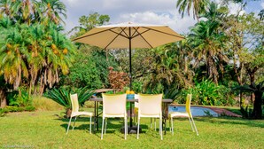 An outdoor patio with a table and chairs, surrounded by lush greenery and palm trees. - The vintage manor (Blantyre)