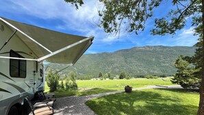 Un véhicule récréatif est stationné dans une zone herbeuse, avec une vue sur les montagnes en arrière-plan.