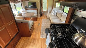 Un intérieur de camping-car compact comprenant un coin cuisine, un espace salon et un téléviseur.