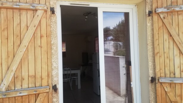 A wooden door with a sliding glass panel leading to a room with a table and chairs. - Maison à la Campagne (Corneilhan)