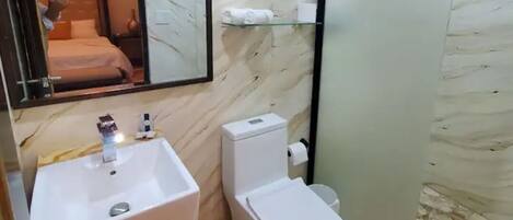 A bathroom with a marble wall, a sink, a toilet, and a shower area.
