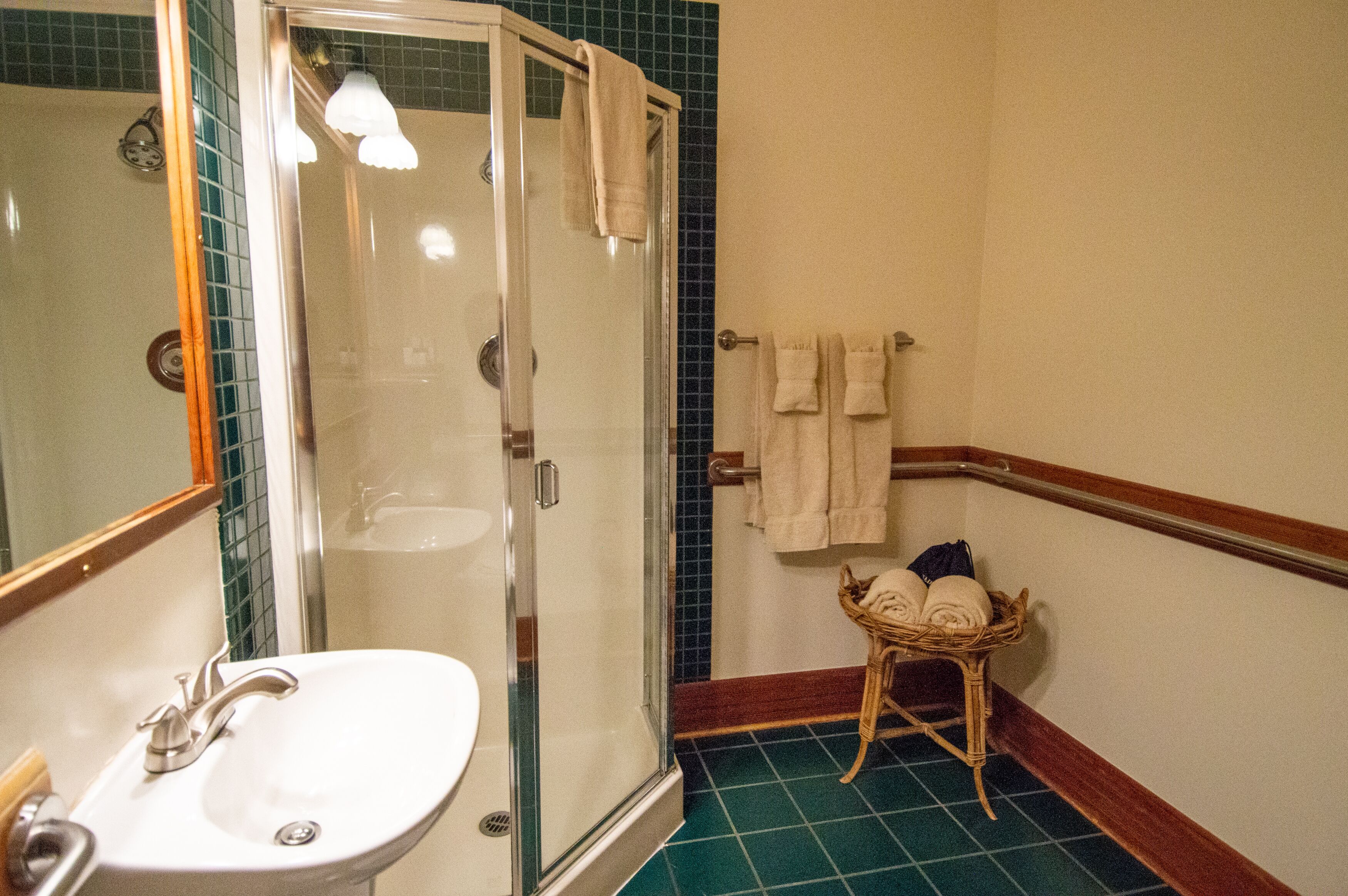 A bathroom with a glass-enclosed shower, a sink, and a wicker basket holding towels.