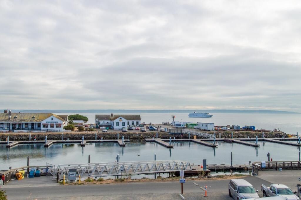 Un puerto costero con barcos amarrados, un ferry y un pequeño edificio con techo de paja.