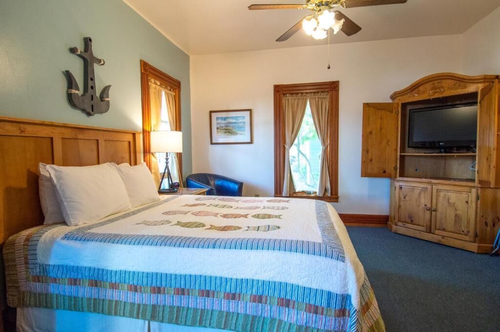 Una habitación de hotel con cama, cabecera de madera, ventilador de techo, televisor y un mueble de madera.