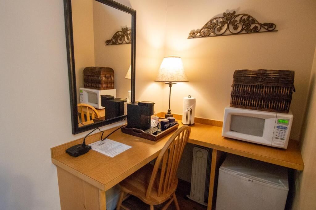 Habitación de hotel compacta con escritorio de madera, microondas, lámpara, refrigerador pequeño y espejo.