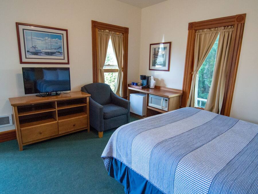 A hotel room with a bed, a desk with a computer, a chair, a television, and a microwave.