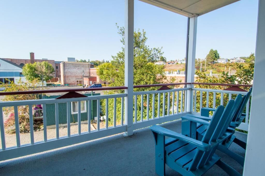 Un balcón techado con sillas Adirondack azules, una mesa y vista a una zona residencial con casas y árboles.