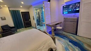 A bedroom with a bed, a dresser, a TV, and a bathroom visible through an open door. - LUX Puerto Caribe Stylish RM- 103 (Aguada)