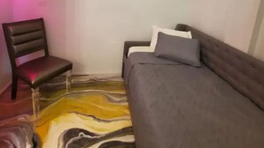 Una habitación pequeña y poco amueblada con una cama, una silla y un televisor en la pared.