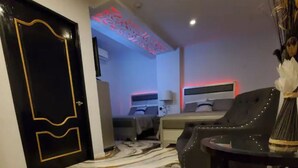 Habitación de hotel con piso de diseño de mármol, puerta negra con detalles dorados, cama con cabecera, mesita de noche y una silla.