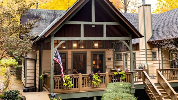 Una baita con rivestimento in legno, un portico con piante e una bandiera americana.