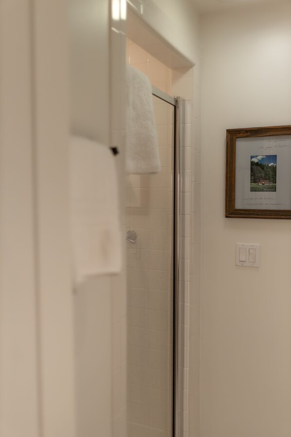 Un baño con mampara de vidrio, un cuadro en la pared y una toalla colgada en la puerta.