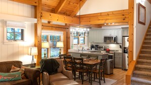 Un'ampia zona giorno con soffitto in legno, un tavolo da pranzo con sedie, una cucina con elettrodomestici moderni e una scala.