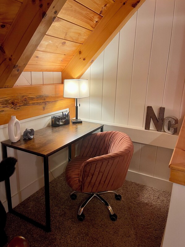 A small office space with a wooden desk, a cushioned chair, a desk lamp, and a white wall with a large 'N' decoration.