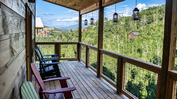 Une terrasse en bois, dotée de chaises Adirondack, et offrant une vue sur une zone boisée avec des maisons visibles au loin.