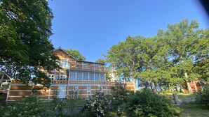 Ein zweistöckiges Holzhaus mit Balkon, umgeben von üppigem Grün und Bäumen.