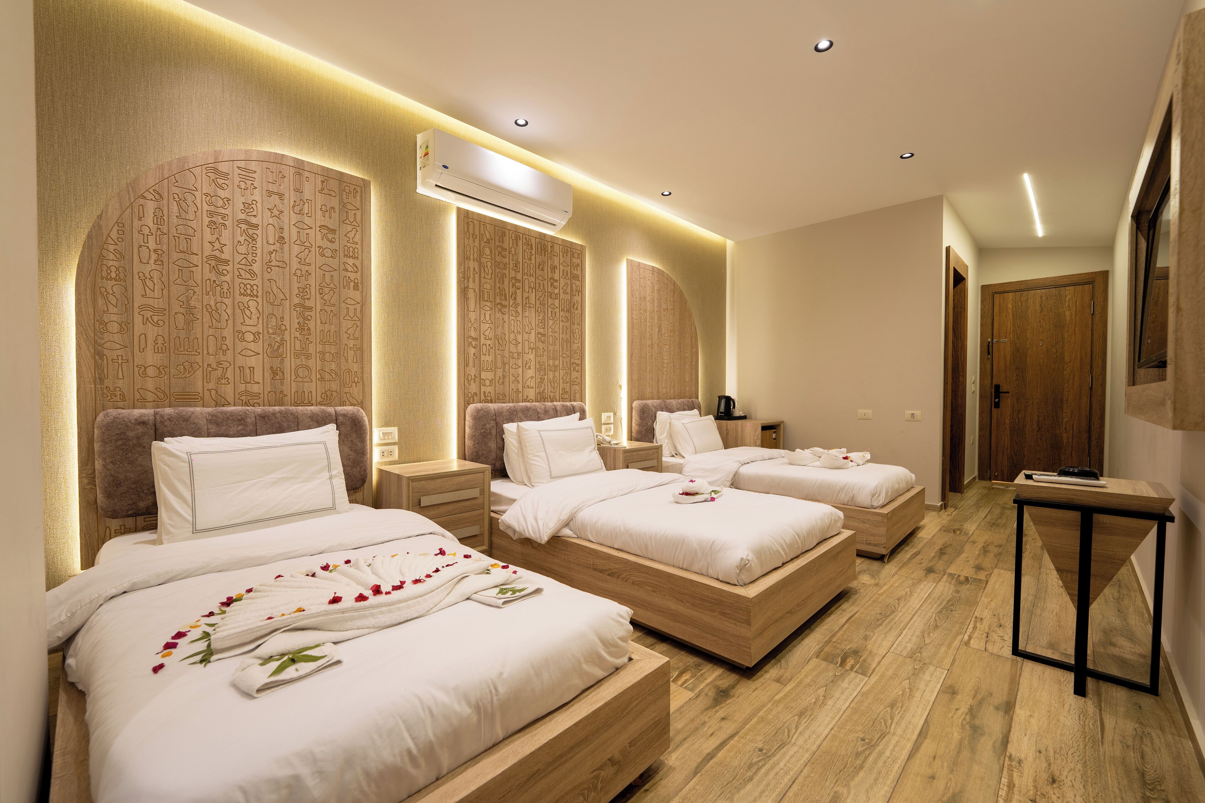 A hotel room with three beds, wooden headboards, and a small table.