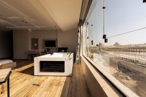Une chambre d’hôtel moderne dotée d’une grande fenêtre, d’un plancher en bois, d’une baignoire blanche et d’un téléviseur à écran plat.