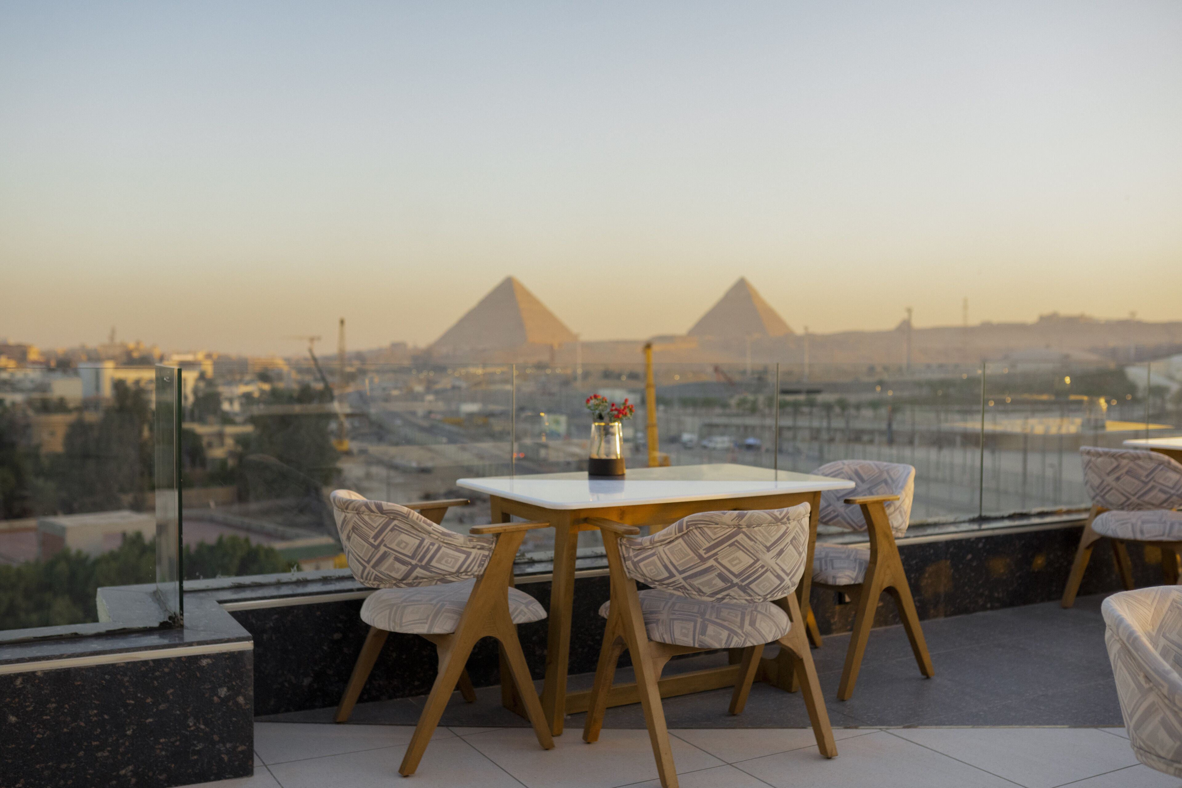 A terrace with a table and chairs, overlooking a cityscape with pyramids in the background.