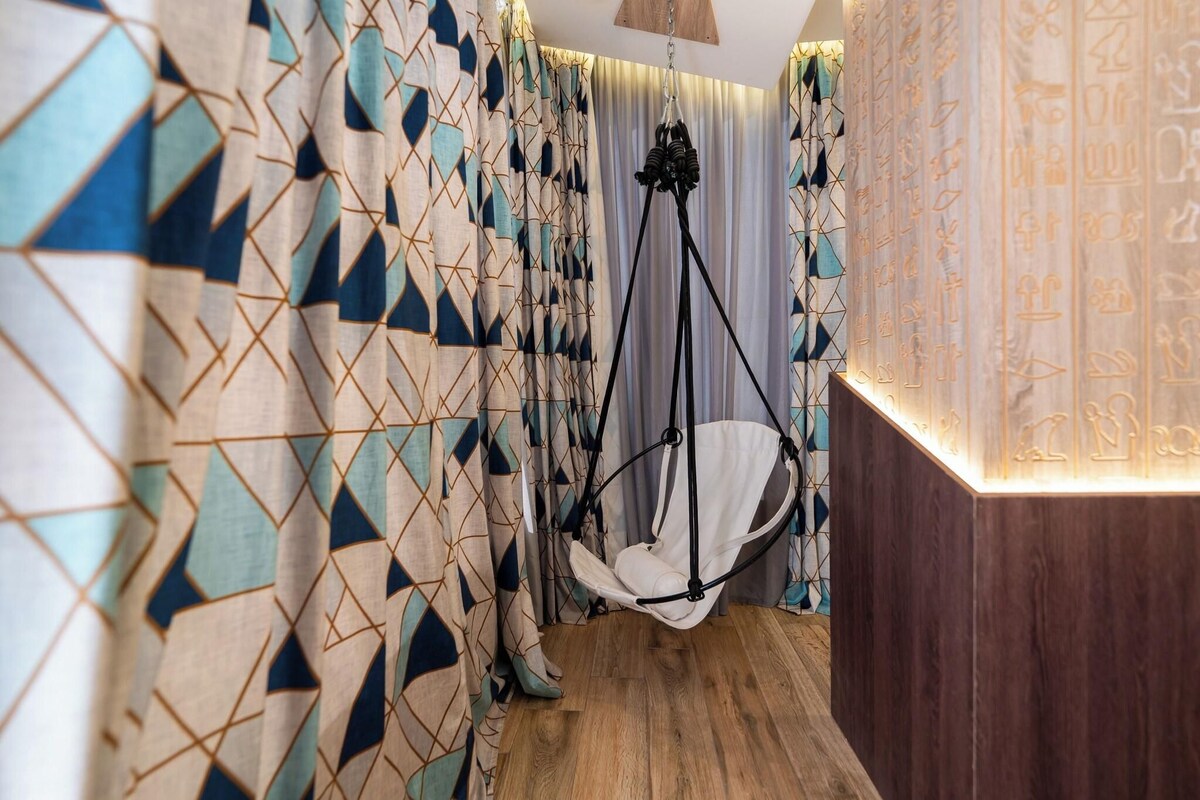 Une pièce avec des rideaux à motifs géométriques, un fauteuil suspendu et un plancher en bois.