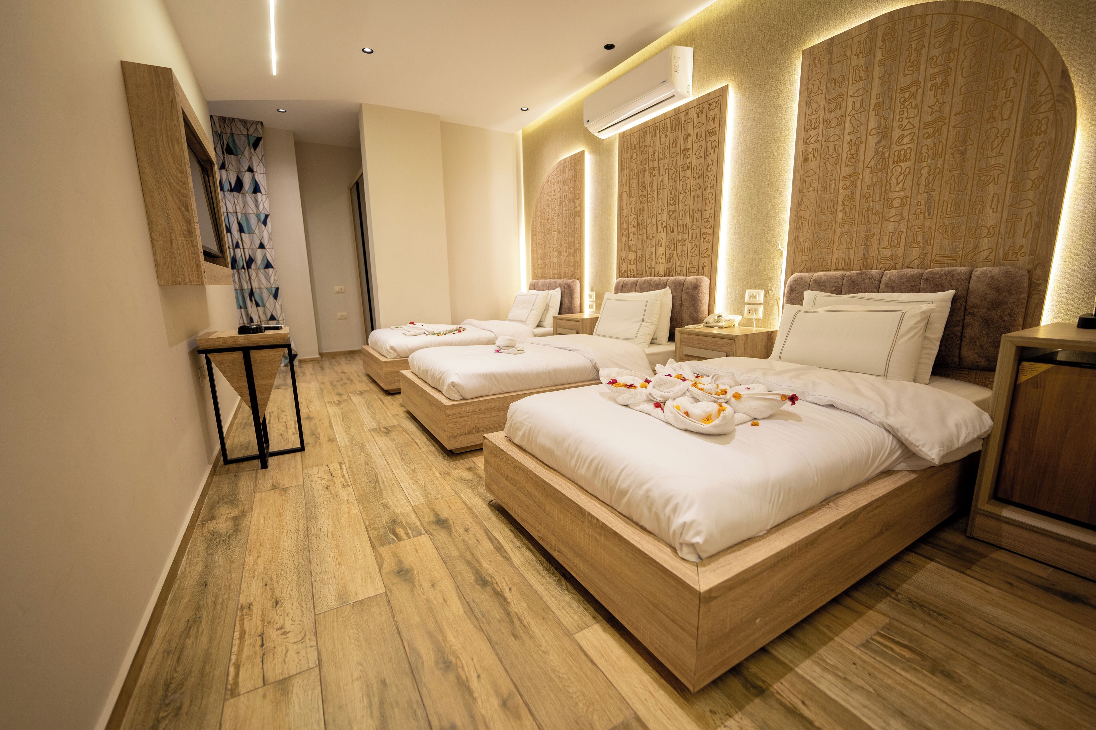 Habitación de hotel con tres camas, suelo de madera y una pared con jeroglíficos.