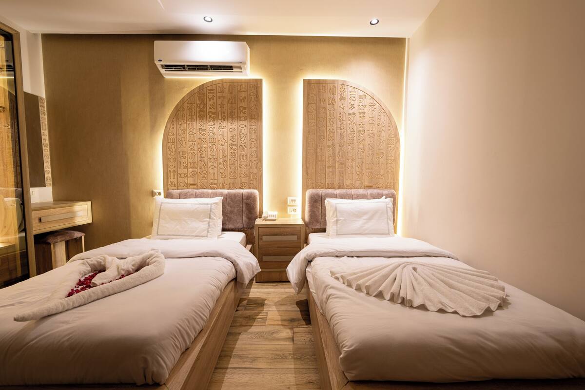 A hotel room with two beds, a wooden floor, and a wall with hieroglyphs.