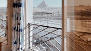 A room with a large window overlooking a pyramid and a construction site. - Royal Great Pyramid INN (Giza)