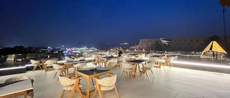 Eine Dachterrasse mit Tischen und Stühlen, einem Zelt und Blick auf die nächtliche Skyline.