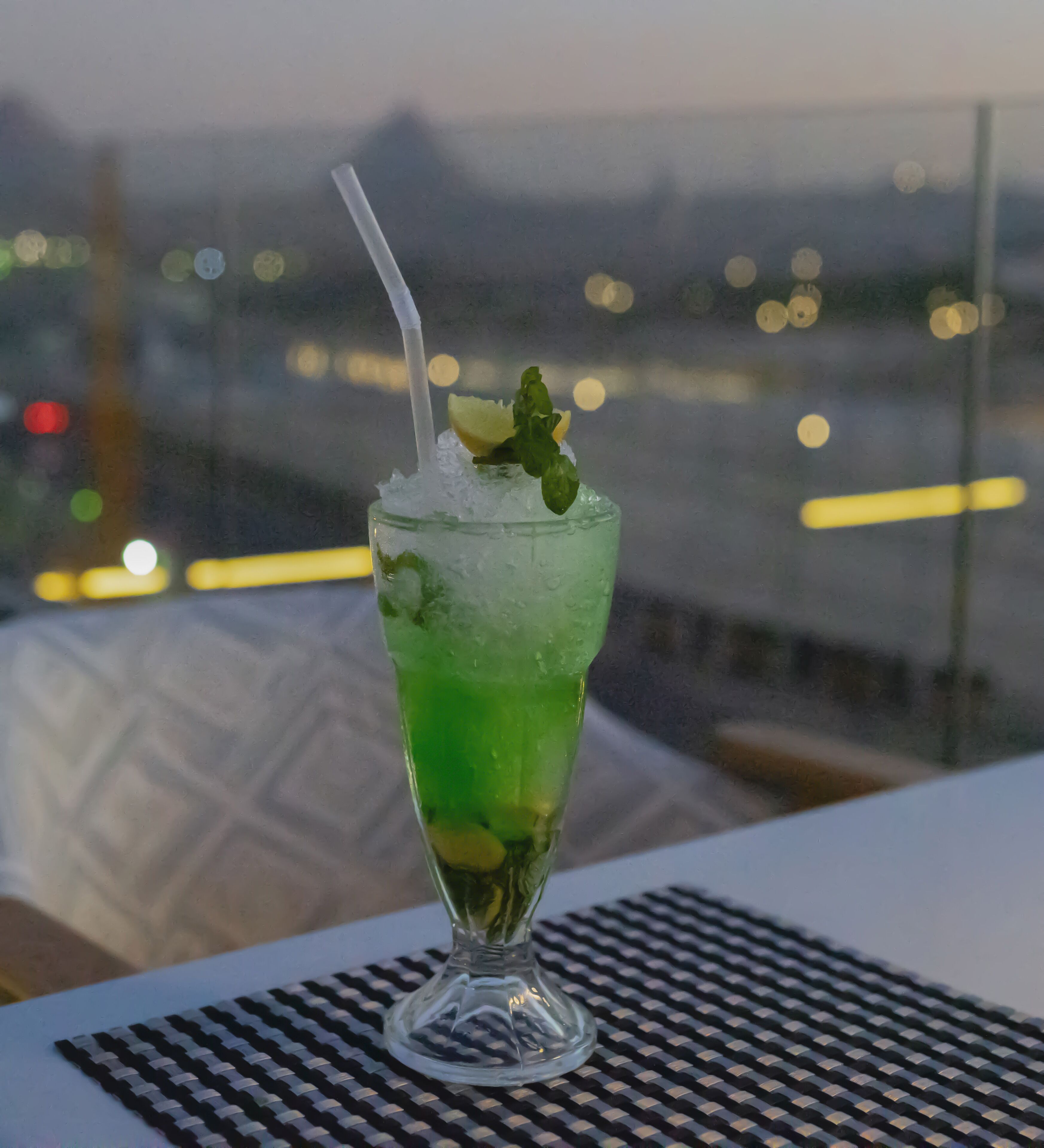 Ein Cocktailglas mit Strohhalm, garniert mit einer Limettenscheibe und Minzblättern, auf einem Tisch mit gemustertem Tischset.