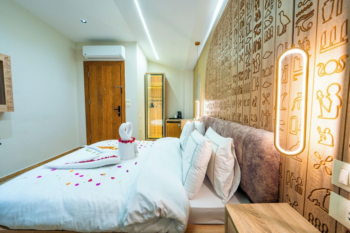 A modern hotel room with a neatly made bed, a wooden wardrobe, and a wall with decorative patterns.