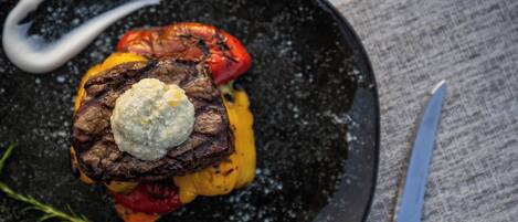 Bife com um pedaço de manteiga por cima, servido em um prato preto com uma faca ao lado.