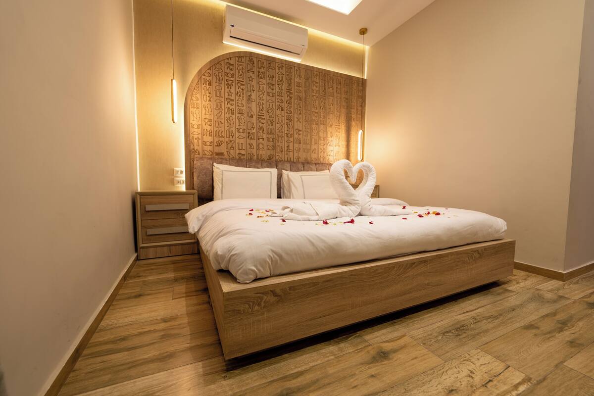 A modern bedroom with a wooden bed frame, a wall-mounted air conditioner, and a unique wall design.