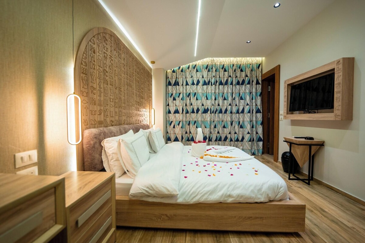 Une chambre moderne avec un lit en bois, une table de chevet, un téléviseur fixé au mur et un rideau à motifs.