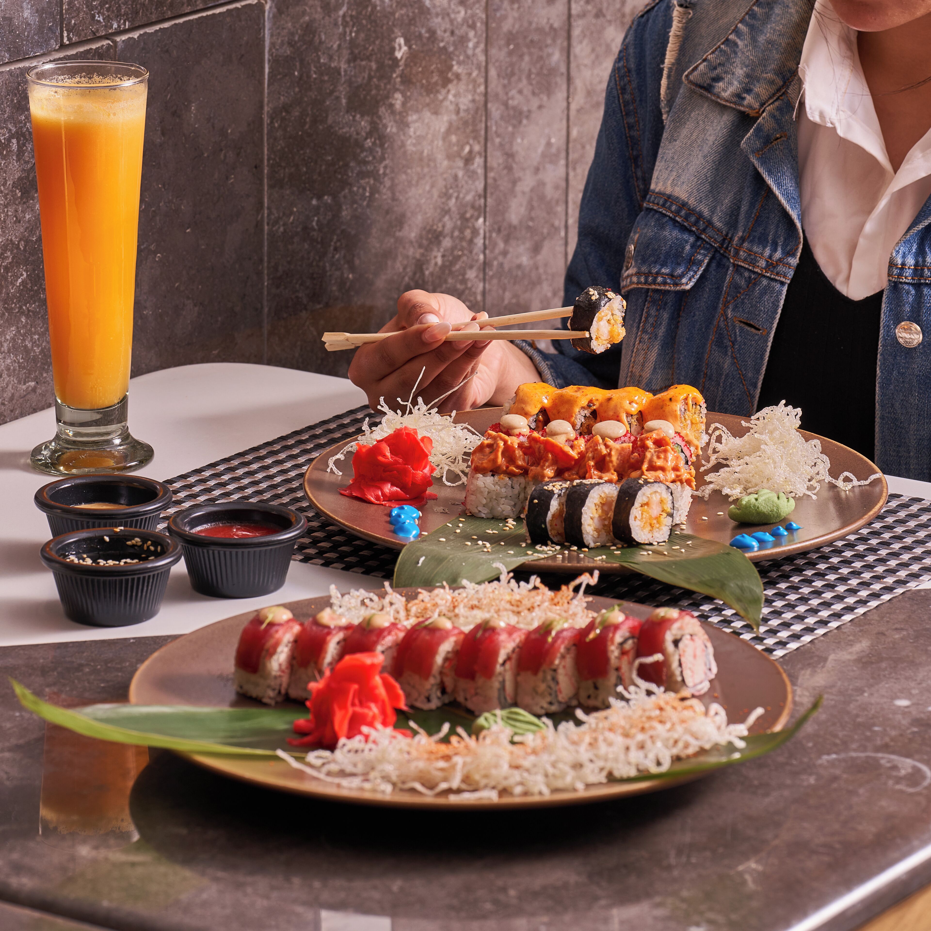 Une table à manger avec différents plats de sushis, un verre de jus d’orange et de petits récipients contenant des condiments.