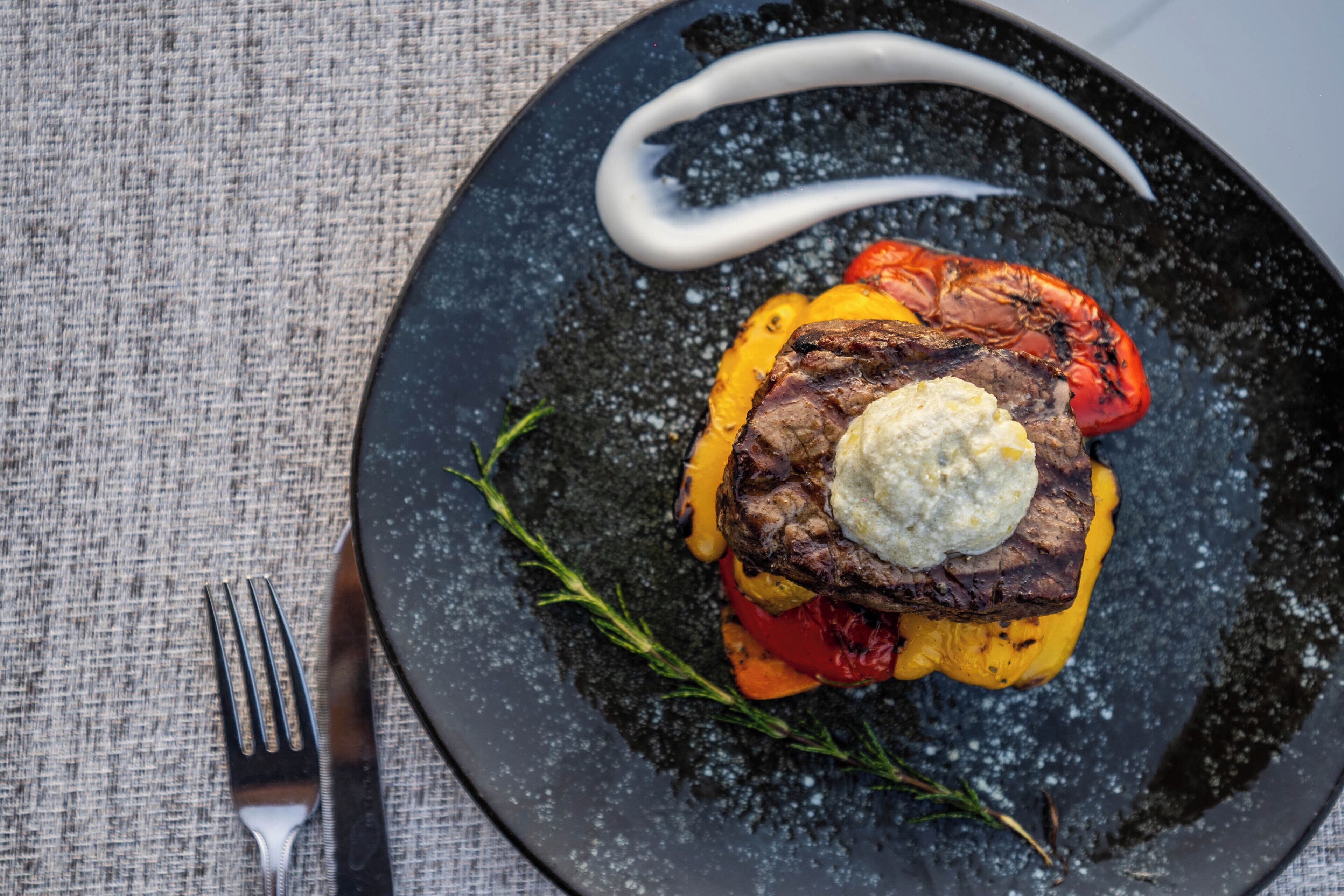 A plate with grilled steak, vegetables, and a dollop of sauce.