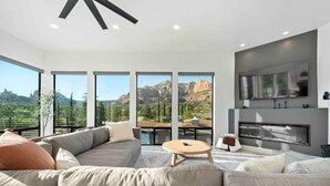 A modern living room with a large sectional sofa, a round coffee table, and a fireplace. Large windows offer a view of a mountainous landscape. - Ultimate Uptown Home Epic Views Private Pool and Spa (Sedona)