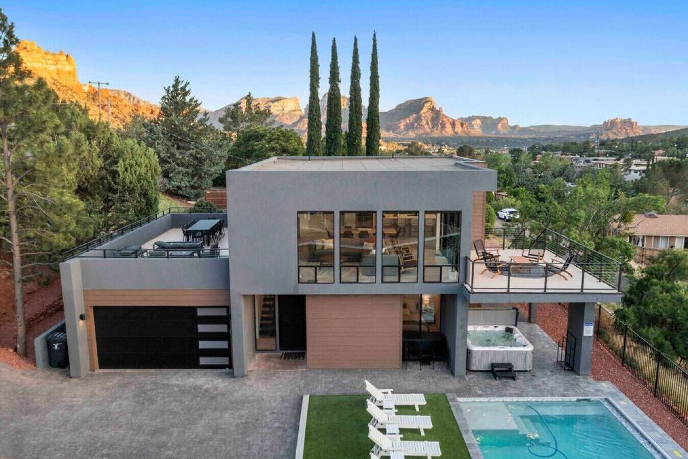 Una casa moderna de dos pisos con garaje, piscina y patio con mobiliario exterior.