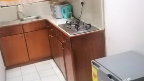 A compact kitchen with wooden cabinets, a sink, a toaster, and a refrigerator. - Vacation Inn Hotel (Accra)