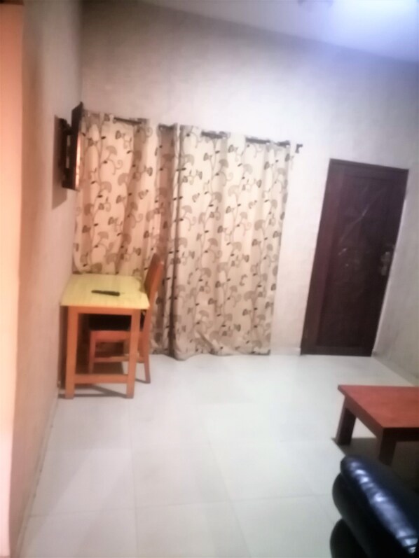 Una habitación pequeña y tenuemente iluminada con una sola silla de madera, una mesita y un sofá de color oscuro.