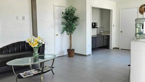 A modern living room with a glass coffee table, a black leather sofa, and a potted plant.