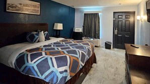 A hotel room with a large bed, a desk, a chair, a TV, a lamp, a window with curtains, and a door.