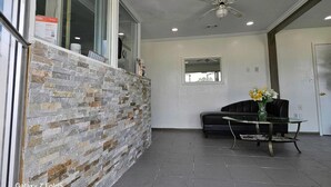 A modern interior with a stone wall, a ceiling fan, a glass table with a vase, and a black sofa.