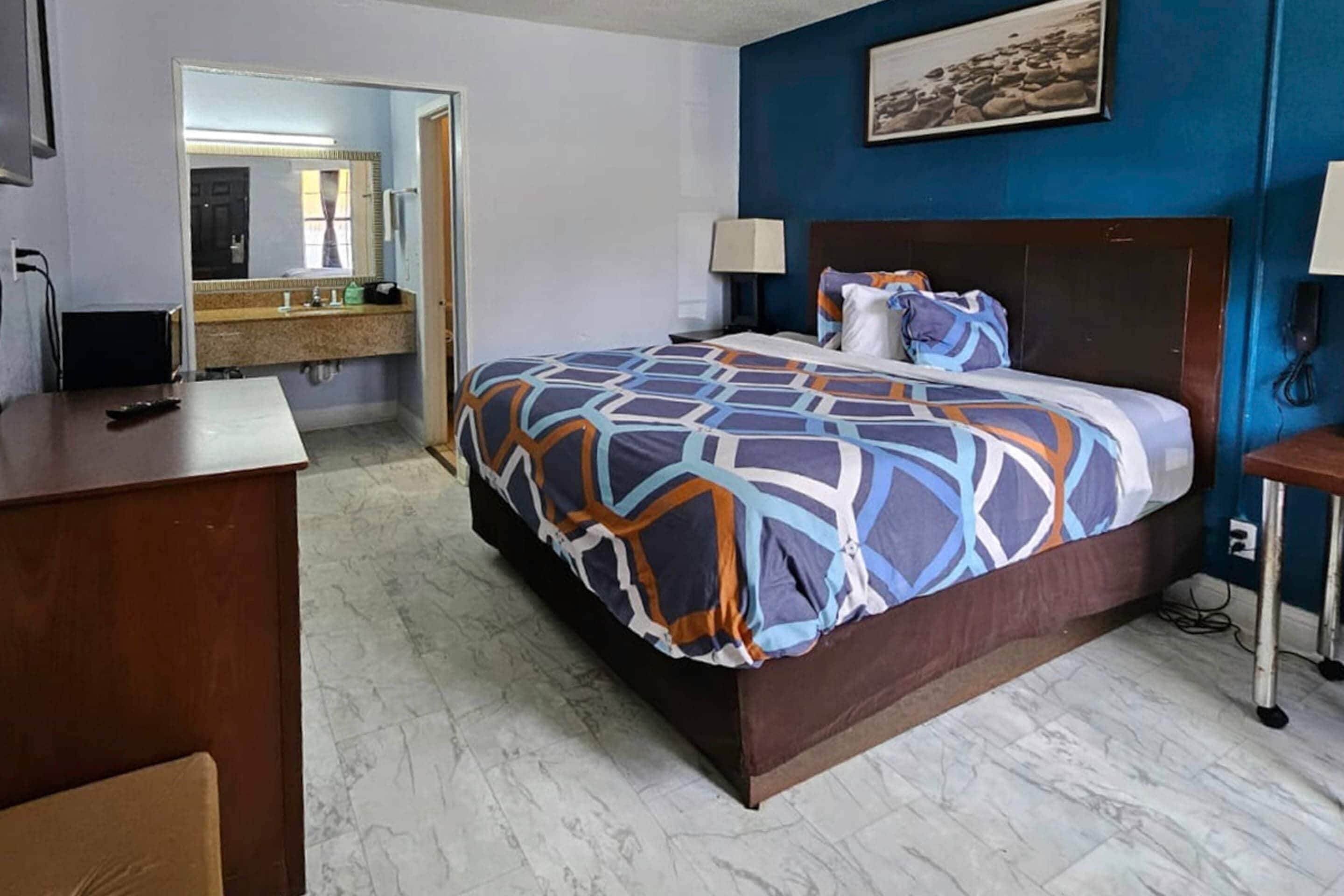 Une chambre d’hôtel avec un grand lit, un bureau, un miroir et une salle de bain équipée d’un lavabo et d’un miroir.