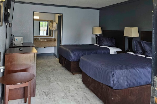 A hotel room with two beds, a desk, a chair, a mirror, and a television.