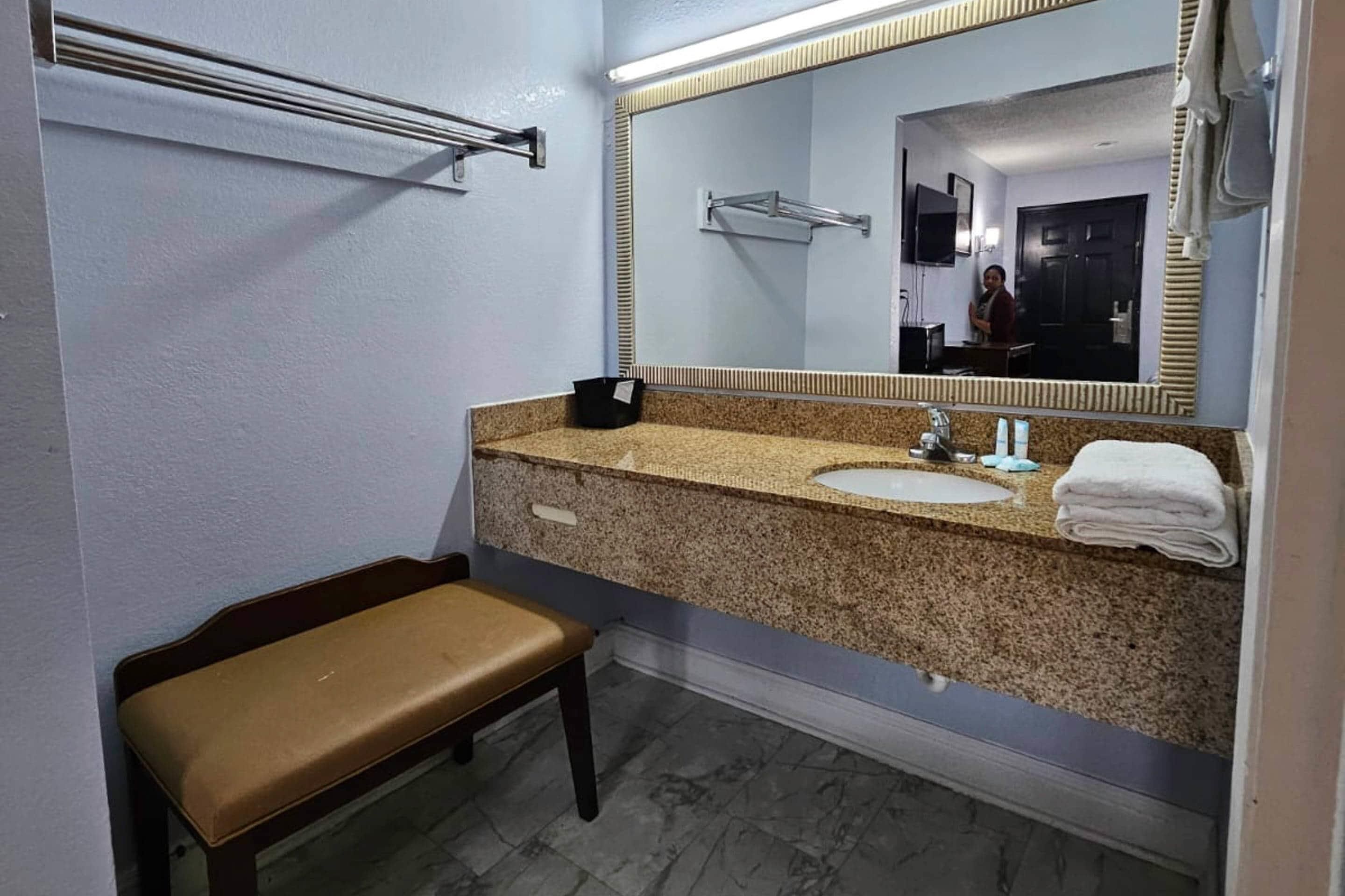 A bathroom with a bench, a sink, a mirror, and a towel rack.