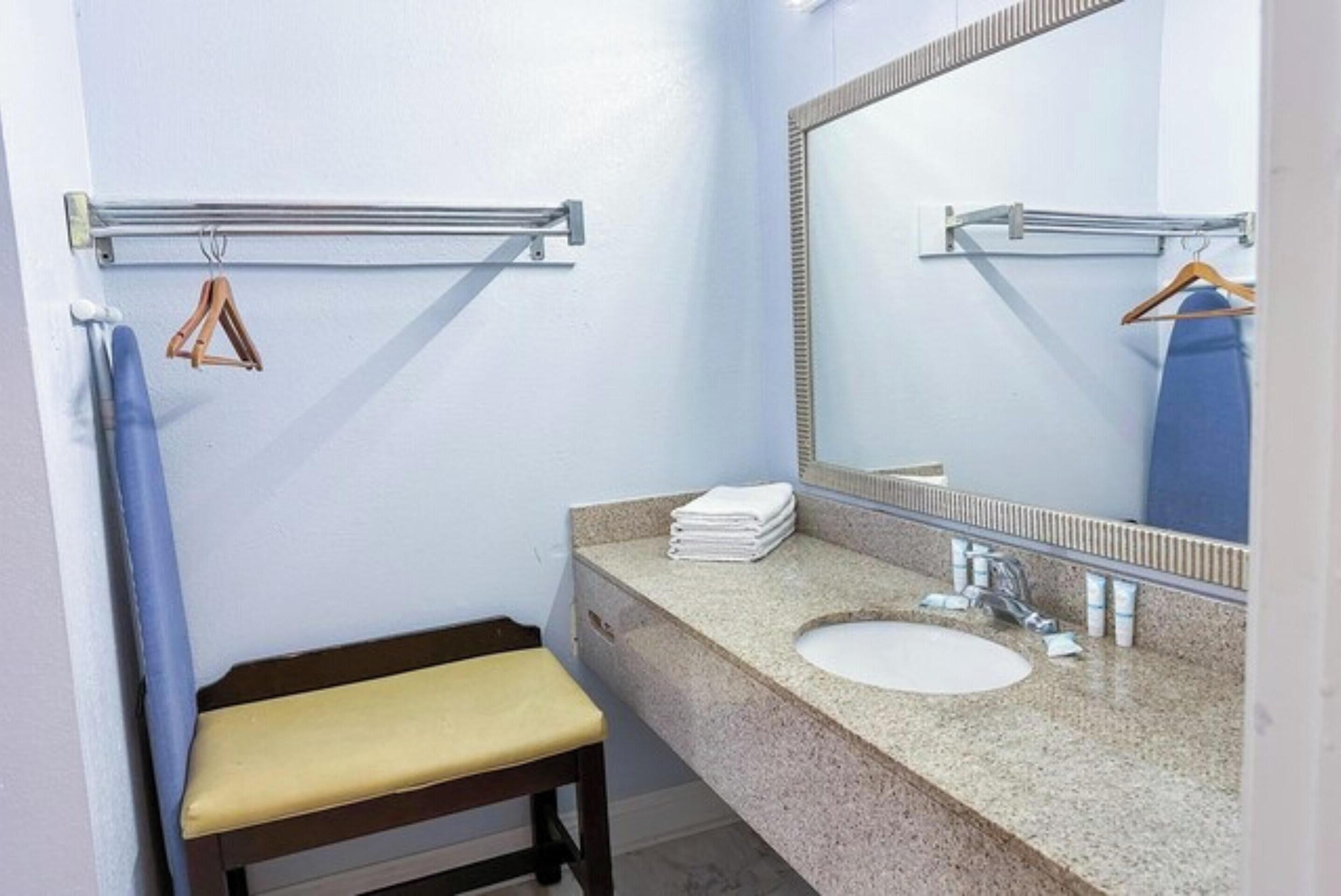 A bathroom with a sink, mirror, towel rack, and bench.