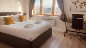 A hotel room with a large bed, a desk, and a view of the city through a window. - Spacious 2 Bedroom City pad in Old Street London (London)