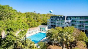 Un hotel con piscina rodeado de exuberante vegetación, una torre de agua al fondo y un edificio moderno con balcones.
