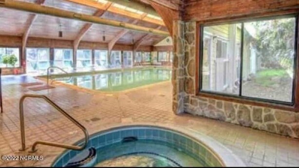 Una piscina interior con pared de piedra y techo de madera, ventanas amplias y vistas despejadas al exterior.